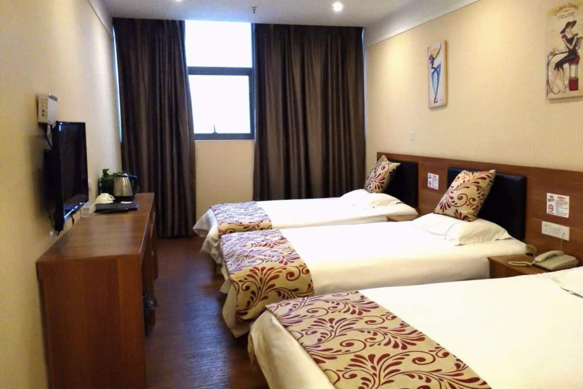 A hotel room with two single beds, a wooden desk with a telephone, a television, and a window with curtains.