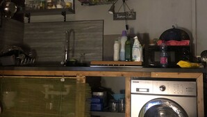 A compact kitchen with a built-in washing machine, a drying rack, and shelves with various kitchen items. - Chalet D'Azaé, from relaxation to escape one step! (La Rivière, Saint-Louis)