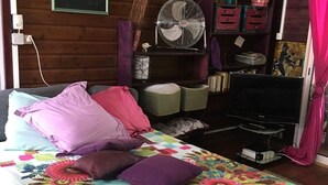 A bedroom with a bed, pillows, a fan, a TV, and wooden walls. - Chalet D'Azaé, from relaxation to escape one step! (La Rivière, Saint-Louis)