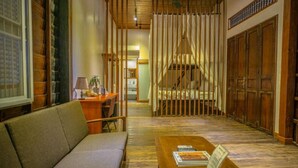 A traditional room with a wooden floor, a sofa, a desk with a lamp, and a bed with a canopy. - The Local Time Village (Siem Reap)