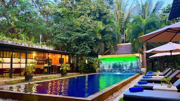 A pool area with lounge chairs and a waterfall feature. - The Local Time Village (Siem Reap)
