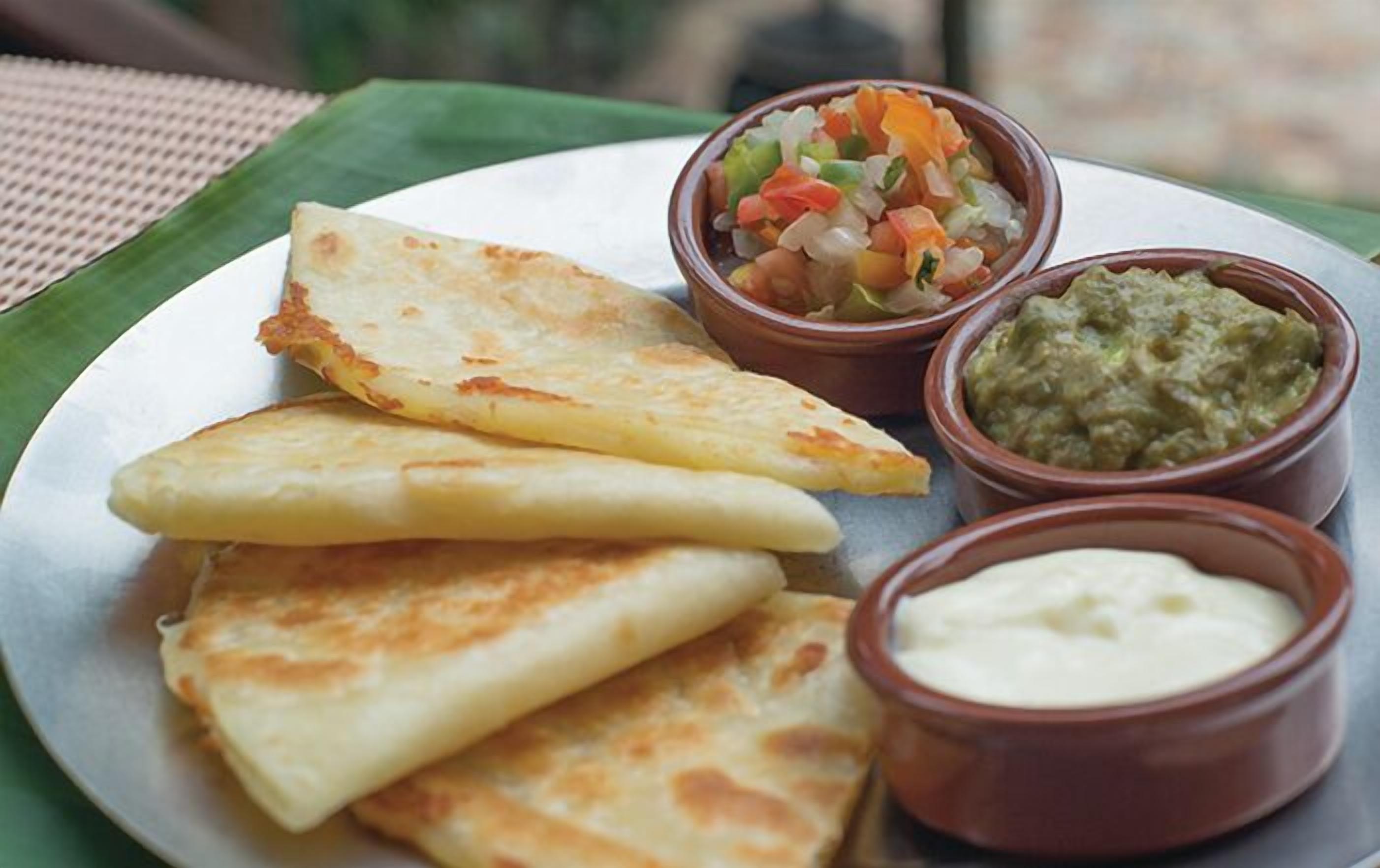 A plate with three pieces of flatbread and two small bowls of dips.