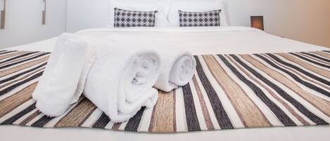 A hotel room with a large bed, white bedding, striped area rug, and a painting of a coastal scene on the wall.