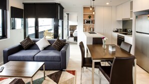 Uma sala de estar moderna com um sofá cinza, uma mesa de centro de madeira e um espaço de jantar com mesa e cadeiras de madeira.