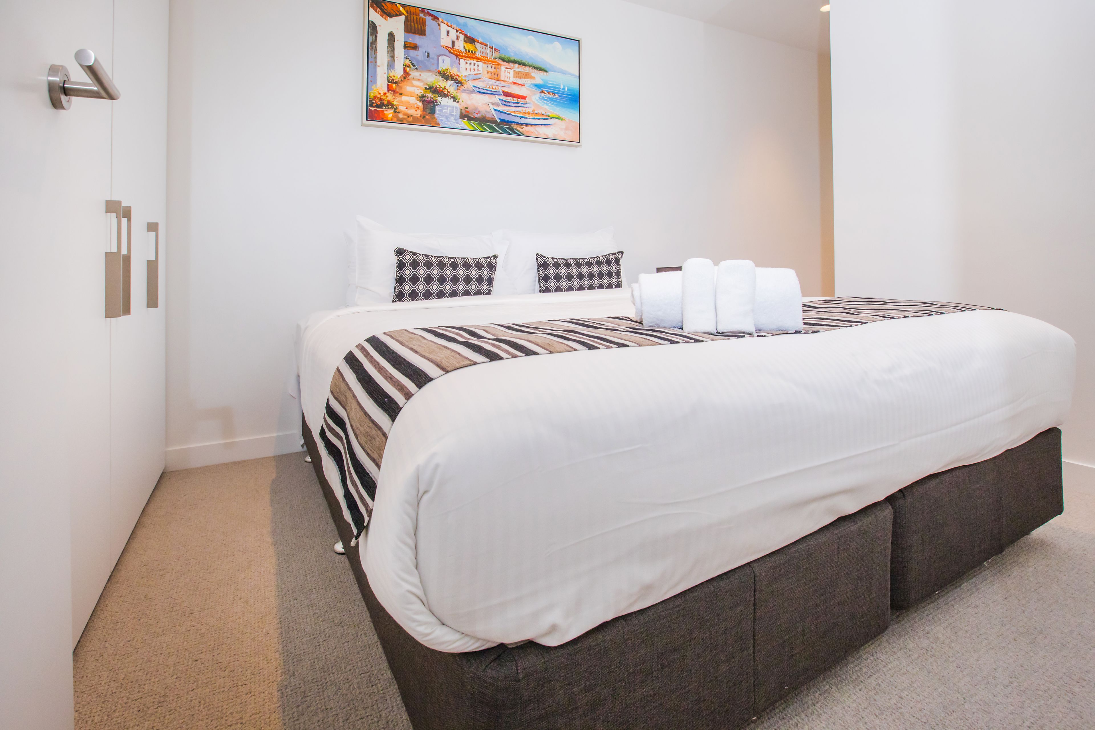 Een moderne hotelkamer met een groot bed, een schilderij van een kustlandschap en een deur met een handgreep.