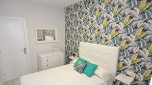 A bedroom with a white bed, a nightstand, a dresser, a mirror, and a wall with a leafy pattern. - Beautiful new house, with terrace / solarium in Arona (Arona)
