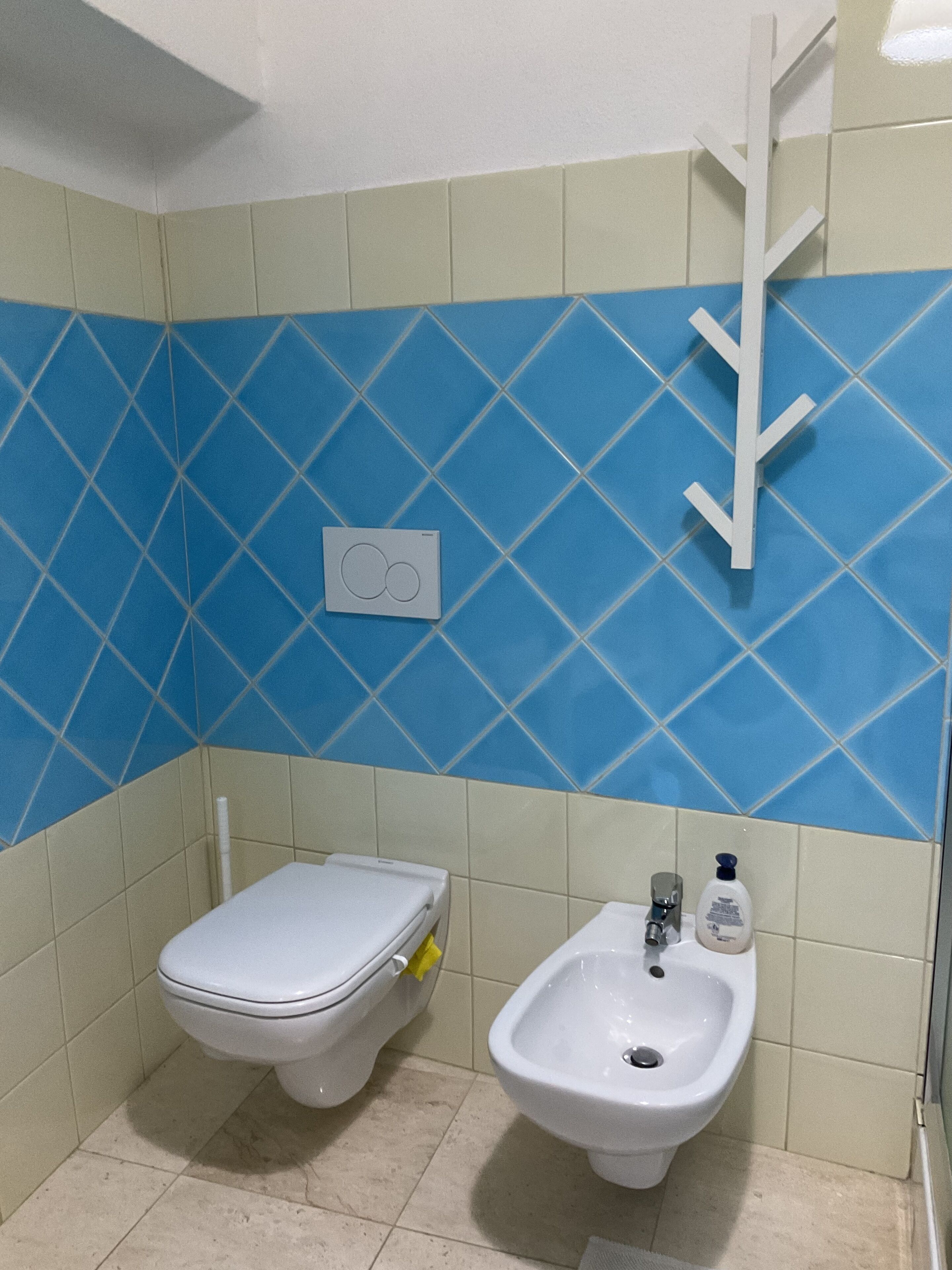 Ein Badezimmer mit Toilette und Bidet, geflieste Wände und einem weißen Handtuchhalter.