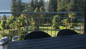 A balcony with a view of a lake, mountains, and a well-maintained garden.