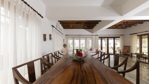 Una larga mesa de madera con sillas, un florero con flores y vistas a un jardín a través de amplios ventanales.