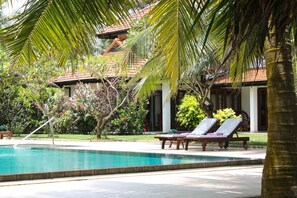 A poolside area with lounge chairs, a palm tree, and a building with a tiled roof.