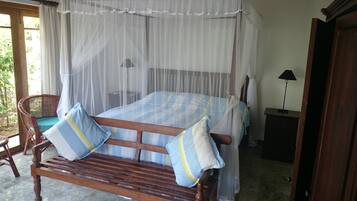 A bed with a canopy, a wooden bench with cushions, a chair, a bedside table, and a lamp.