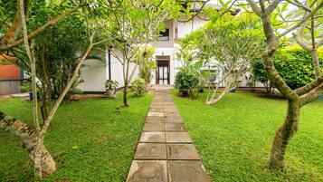 A pathway leading to a building with a door, surrounded by greenery and trees.