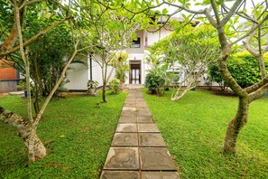 A pathway leading to a building with a door, surrounded by greenery and trees.