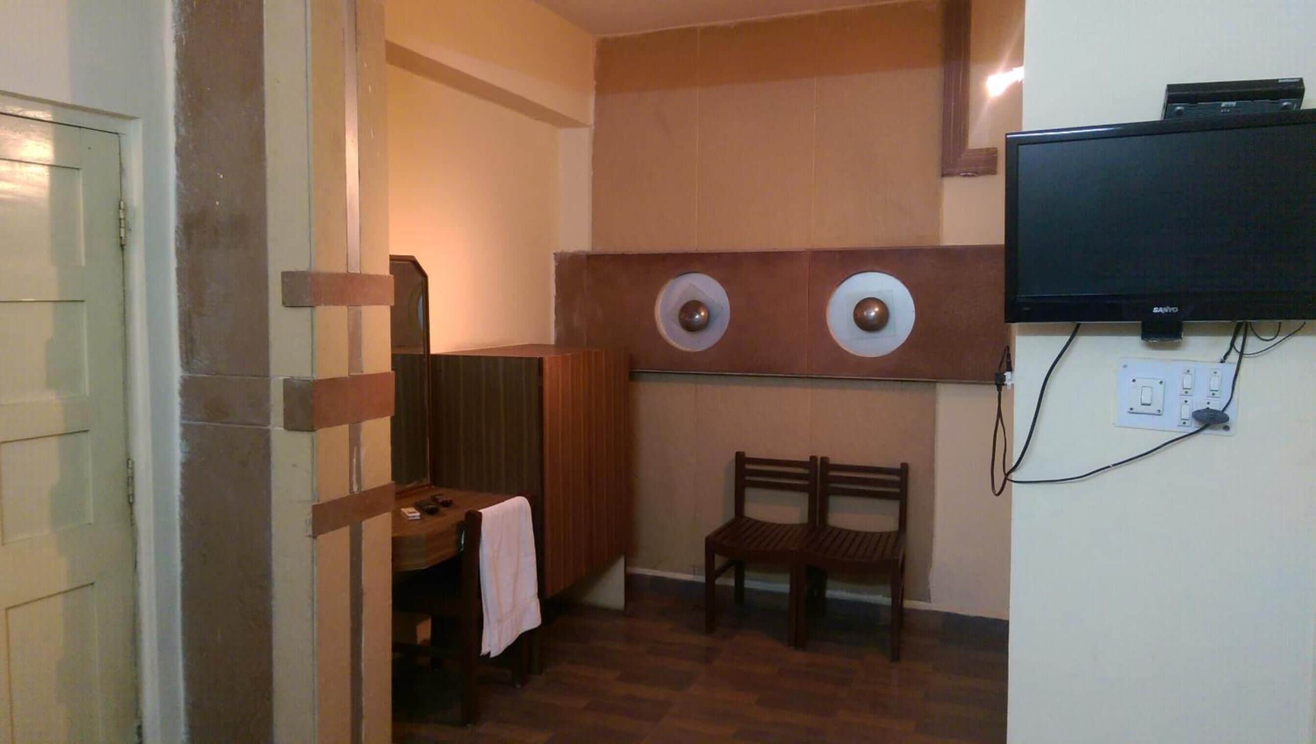A small bathroom with a wooden bench, a mirror, and a television mounted on the wall.