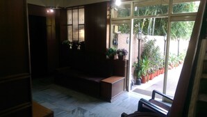 A reception area with a wooden bench, potted plants, and a view of the outside through large windows. - Hotel New Sunder (Indore)