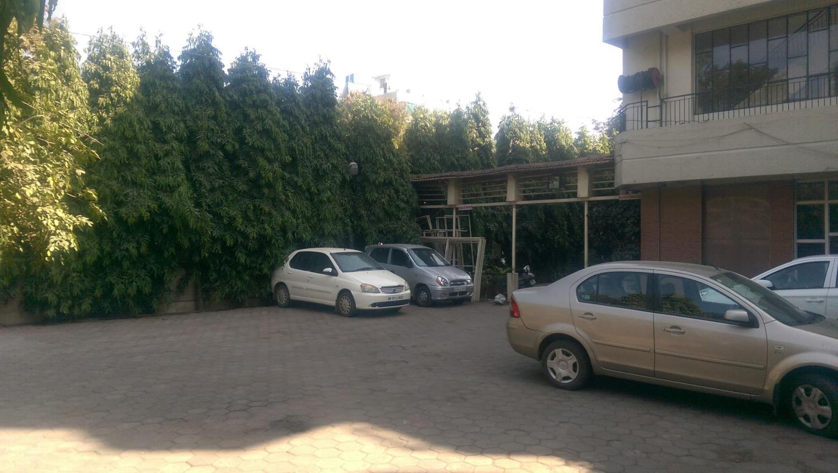 Un estacionamiento con varios coches, un edificio con amplios ventanales y un seto verde frondoso.