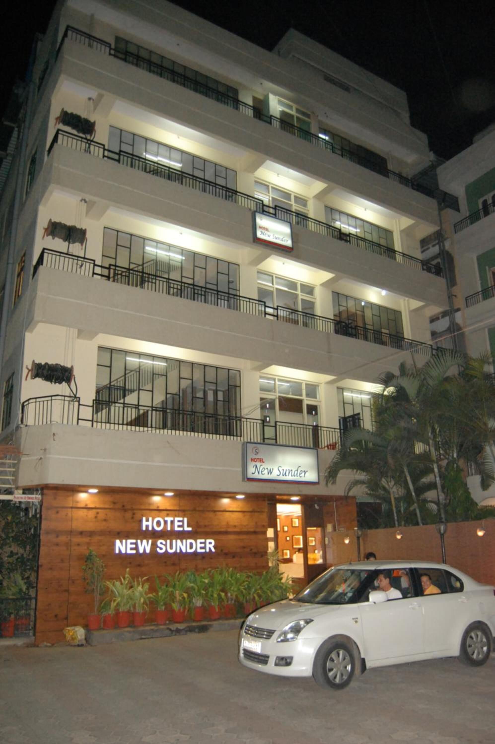 A multi-story hotel with balconies, a sign reading "HOTEL NEW SUNDER," and a white car parked in front.