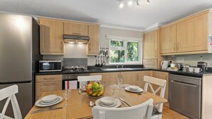 A modern kitchen with wooden cabinets, stainless steel appliances, and a dining area set for four. - Riverside 2 Bed Lodge with Hot Tub. Walk to Lynton Centre. Free Parking. (Lynton)