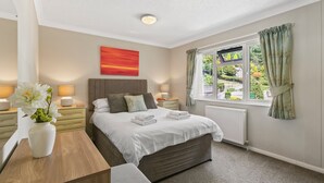 A bedroom with a large bed, bedside tables, a nightstand, a window with curtains, and a painting on the wall. - Riverside 2 Bed Lodge with Hot Tub. Walk to Lynton Centre. Free Parking. (Lynton)