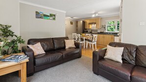 A living room with two brown leather sofas, a wooden coffee table, and a dining area with a white table and chairs. - Riverside 2 Bed Lodge with Hot Tub. Walk to Lynton Centre. Free Parking. (Lynton)