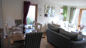 Een eetgedeelte met een houten tafel voor vier personen, een gestreepte stoel en een grijze bank in een lichte woonkamer met uitzicht op het buitenland.