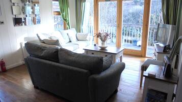 A living room with a grey sofa, a coffee table with a vase, and a television on a stand.