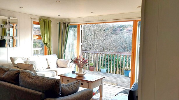 Een moderne woonkamer met een bank, salontafel en uitzicht op een balkon met potplanten.