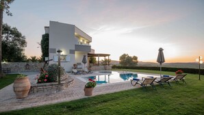 Ein modernes, zweistöckiges Haus mit Pool, Sitzgelegenheit im Freien und einer Steinmauer.