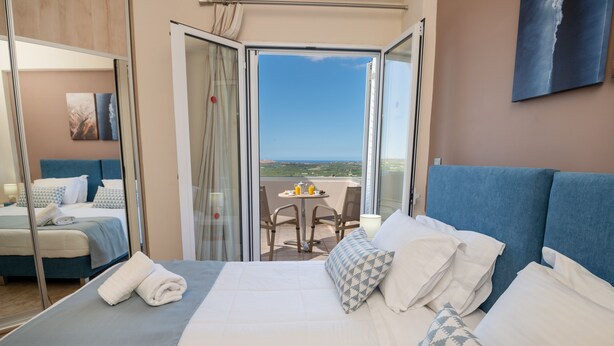 Ein Hotelzimmer mit einem großen Bett, einem Balkon mit Tisch und Stühlen sowie Blick auf die Landschaft.
