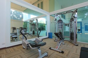 A gym with cardio machines, weight training equipment, and large windows offering a view of the outdoors. - My Resort Huahin by Love Huahin (Hua Hin)