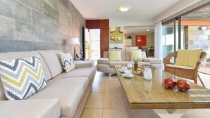 Un salon moderne avec un canapé beige, une table basse en verre et un fauteuil en osier.