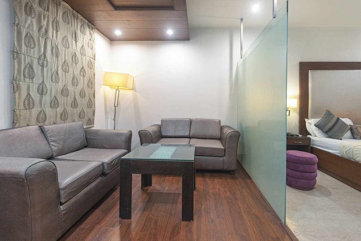 A hotel room with a sofa, a glass-top table, and a bed with a headboard.