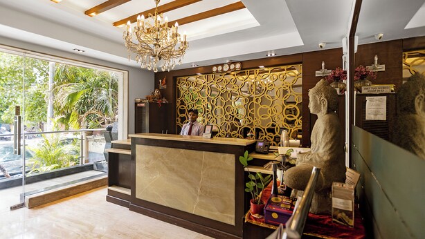 A hotel reception area with a marble reception desk, a chandelier, a receptionist, and a Buddha statue. -  The Grand Vikalp by Saga Hotels (New Delhi)