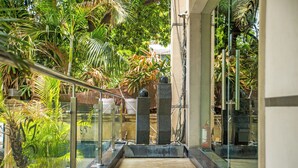 A glass-walled corridor with a marble floor, surrounded by lush greenery and palm trees. -  The Grand Vikalp by Saga Hotels (New Delhi)