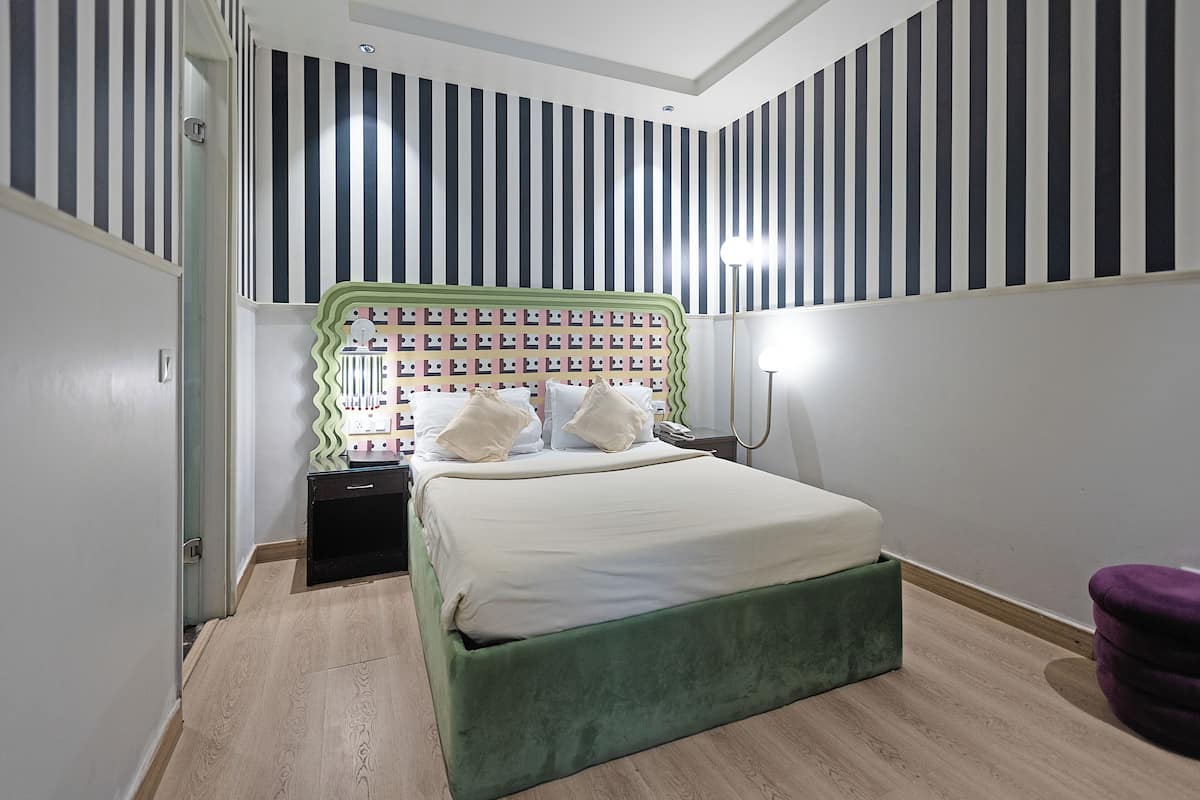 A bedroom with a striped wall, a green upholstered bed, a bedside table, and a purple chair.