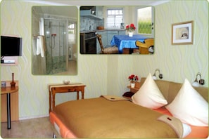 A bedroom with a bed, a TV, a bathroom with a shower, and a kitchen area. - Apartment comfort - Pension Brilke (Ahrenshoop)