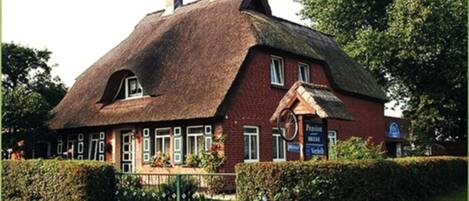 A traditional building with a thatched roof, a sign indicating a pub, and a brick facade.