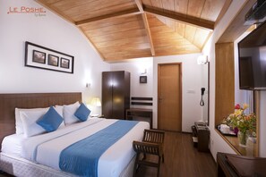 Habitación de hotel con techo de madera, cama con ropa de cama azul, escritorio con silla, armario y televisor.