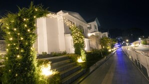 Un sendero flanqueado por un edificio blanco, decorado con luces de adorno y un árbol de Navidad.