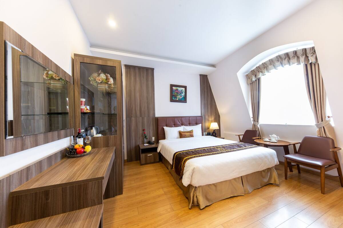 Una habitación de hotel con cama, escritorio con espejo, silla, una mesita y ventana con cortinas.