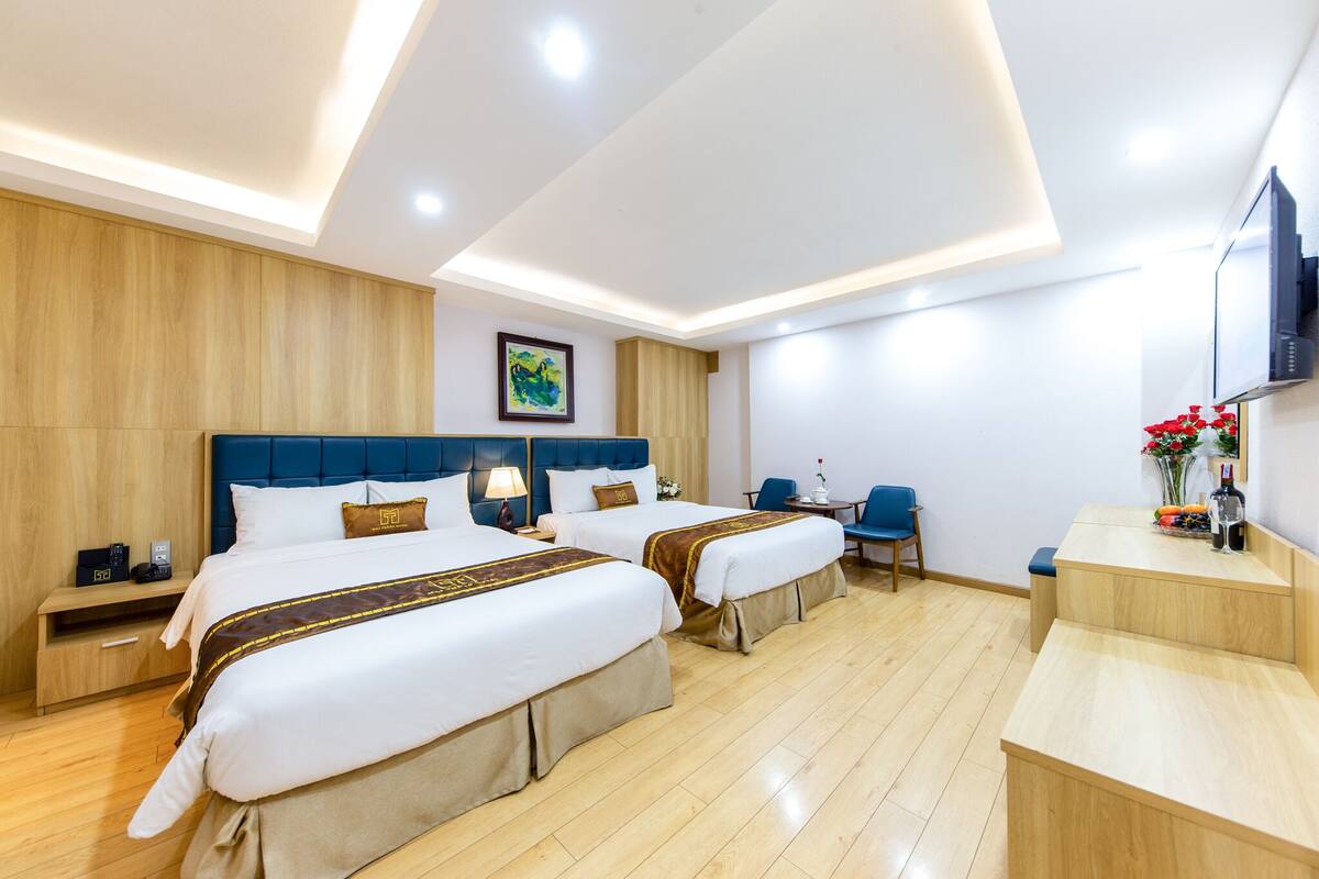 Una habitación de hotel con dos camas, un escritorio, una silla, un televisor y piso de madera.