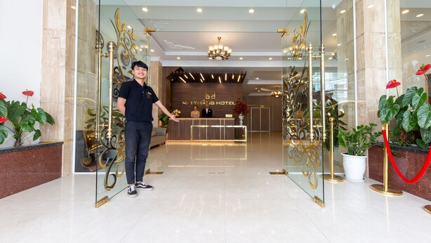 Et hotellets receptionområde med et moderne design, inklusive en receptionsdisk, en lysekrone og potteplanter.