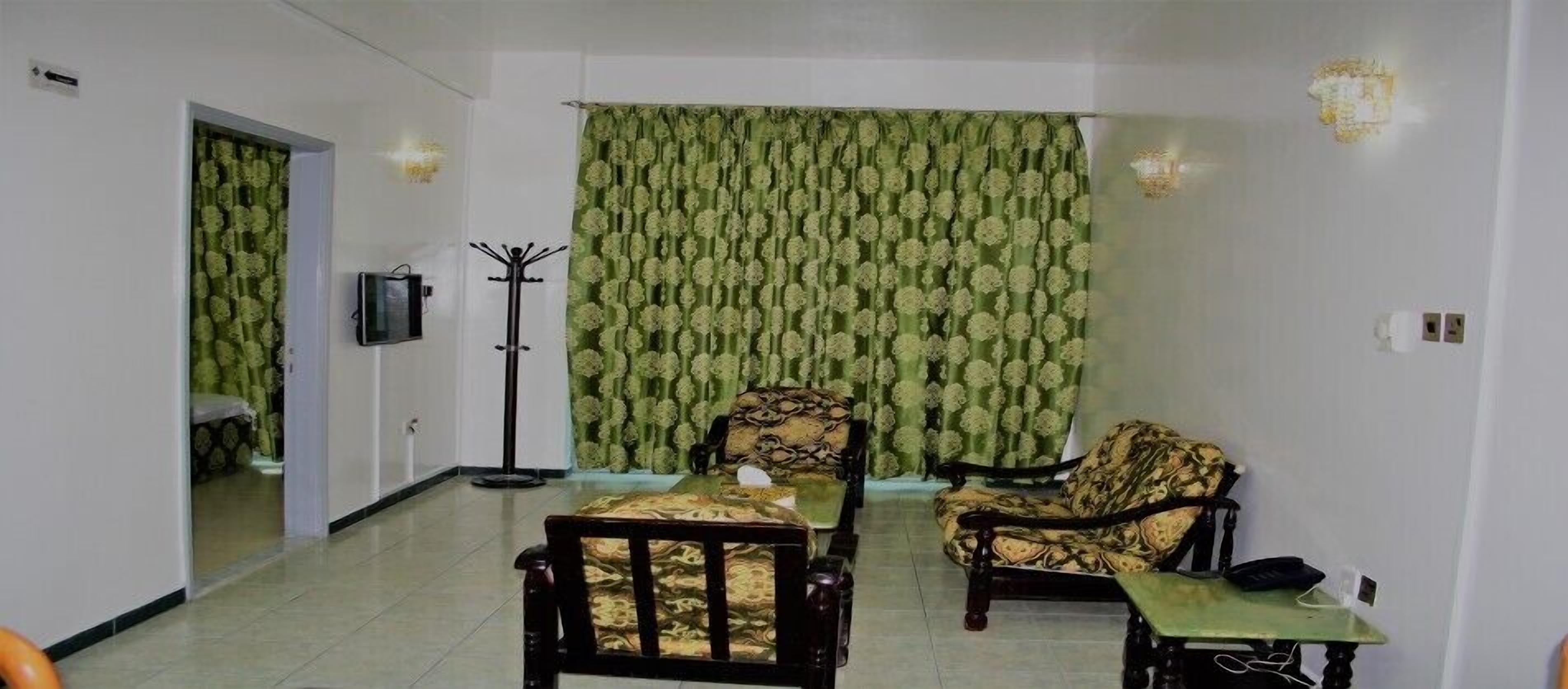 A room with two patterned armchairs, a small table, a coat rack, and a television.