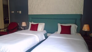 Quarto de hotel com duas camas, uma cadeira vermelha e uma luminária fixada na parede.