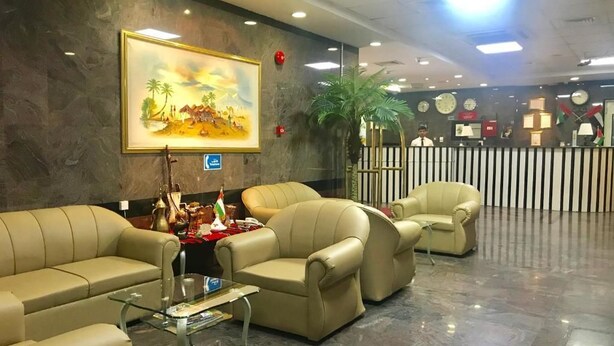 Um hall com sofás de couro, uma mesa de centro de vidro, um quadro na parede, um vaso com planta e um balcão de recepção.