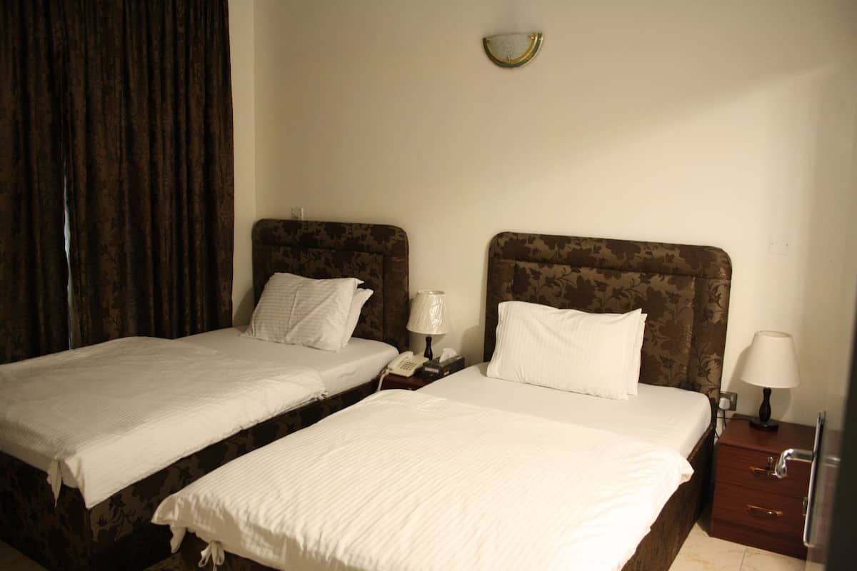 Une chambre d’hôtel avec deux lits simples, une table de chevet avec une lampe et une horloge murale.