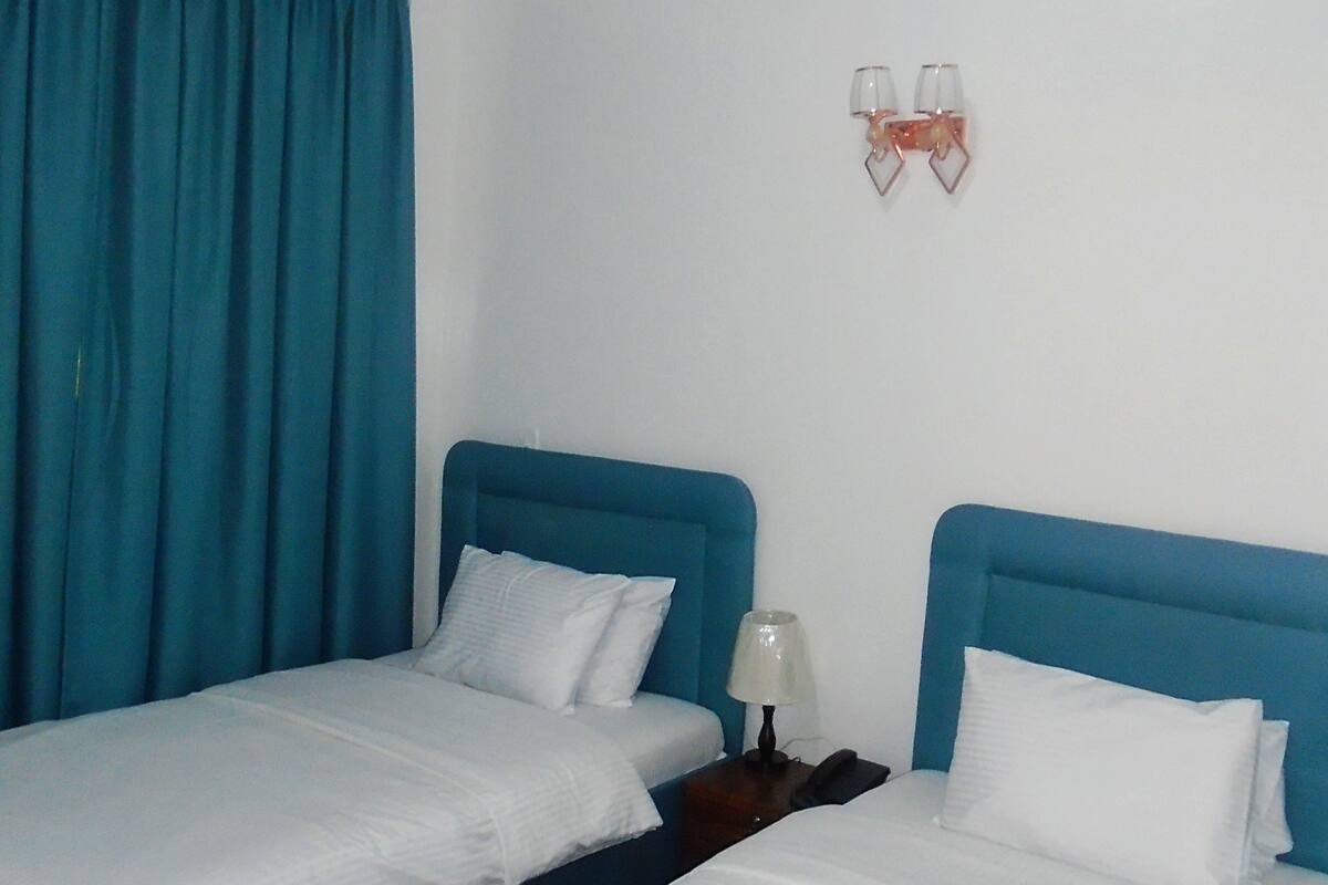 Une chambre d’hôtel avec deux lits simples, une table de chevet avec une lampe et un luminaire fixé au mur.
