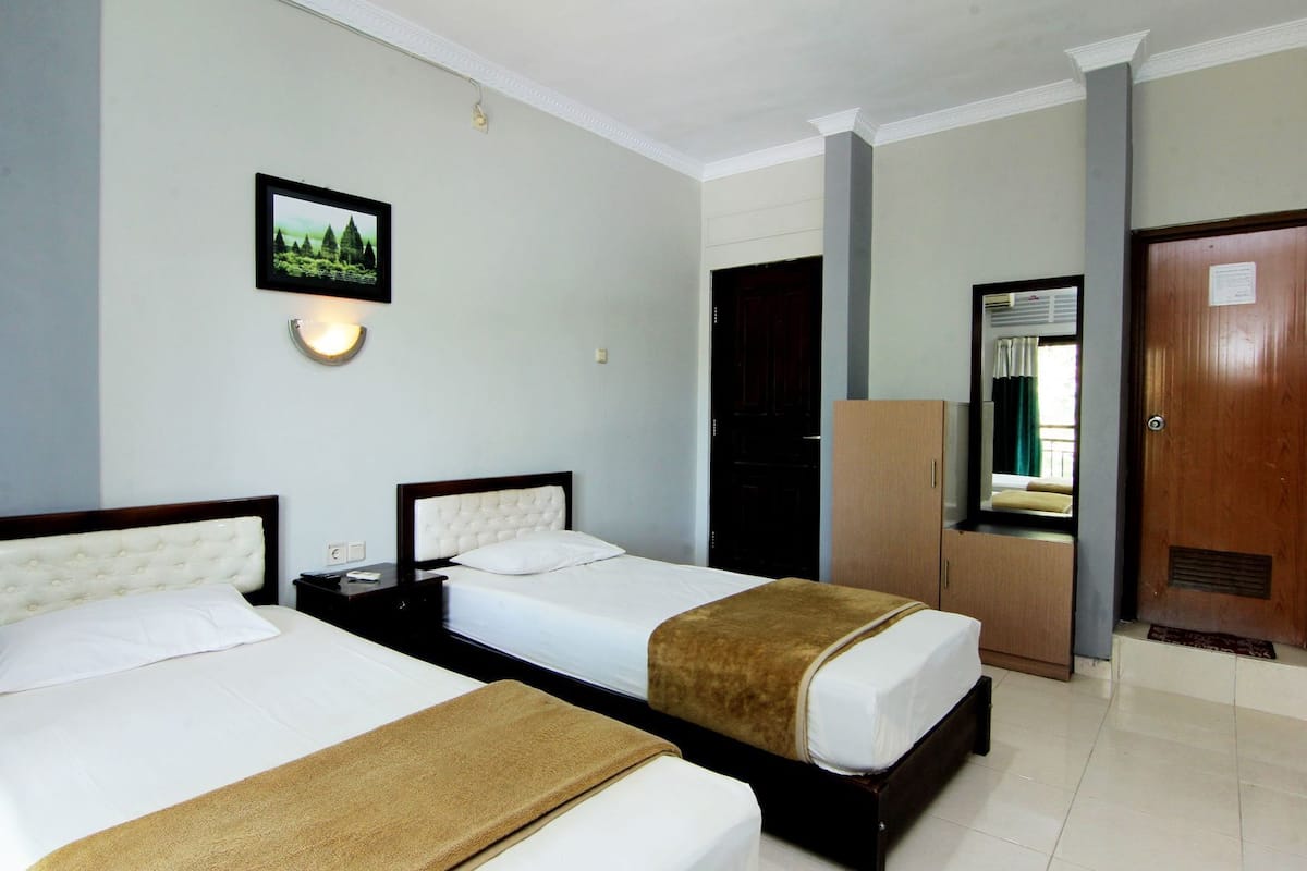 Habitación de hotel con dos camas, un armario, un espejo y un cuadro en la pared.