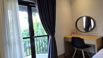A hotel room with a bed, a desk with a chair, a round mirror, and a balcony with curtains.