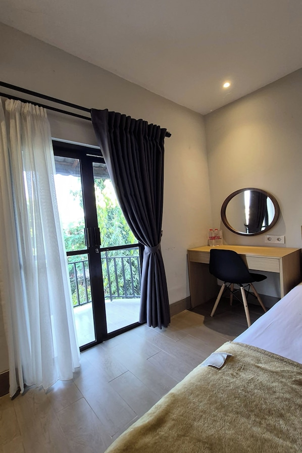 A hotel room with a bed, a desk with a chair, a round mirror, and a balcony with curtains.